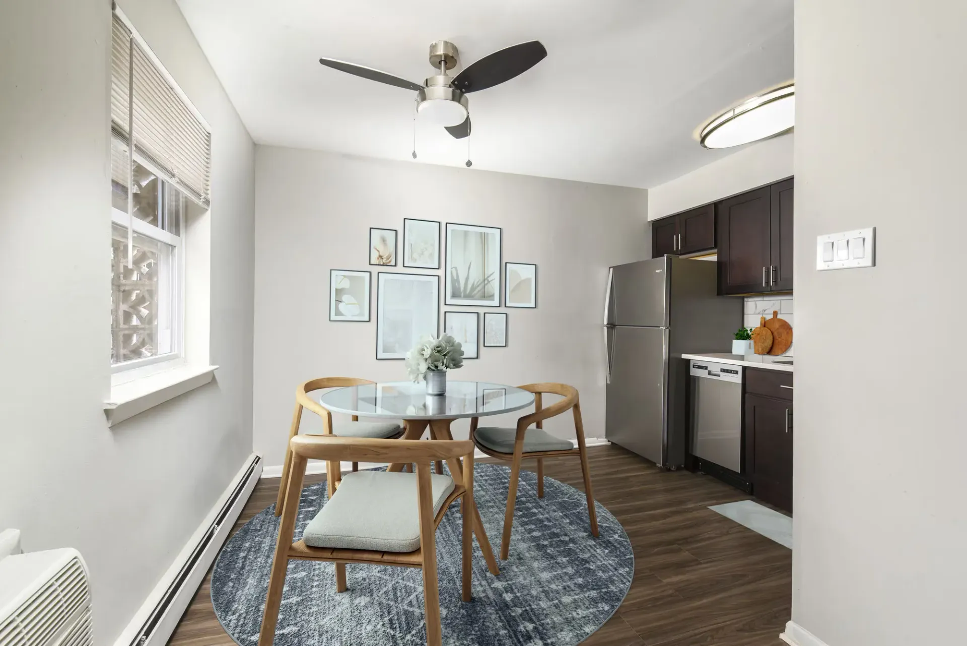 Dining area in a compact apartment with a round glass table, wooden chairs, and stainless appliances.