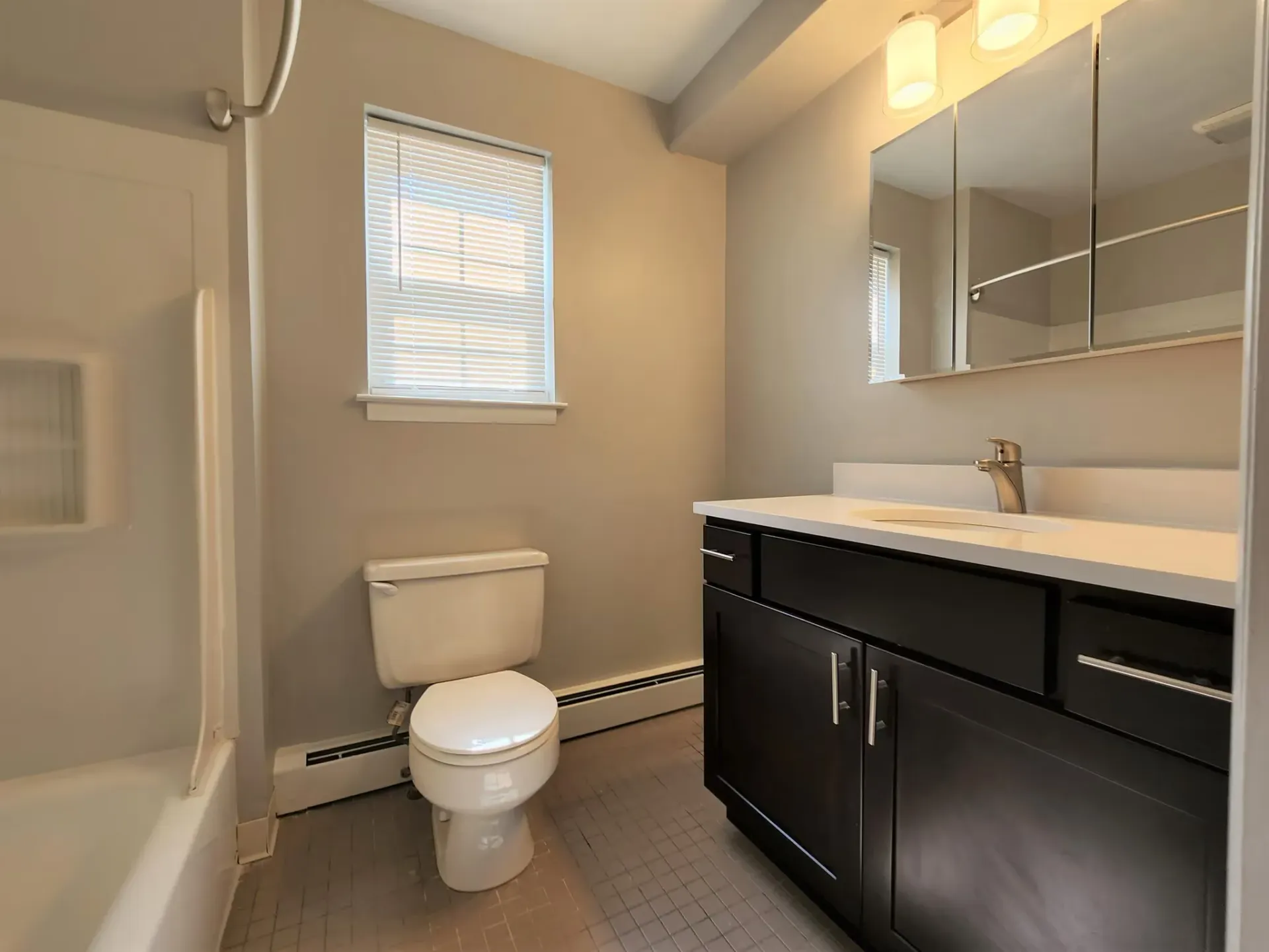 Bathroom in an apartment with a single vanity, mirror, toilet, and shower/tub.