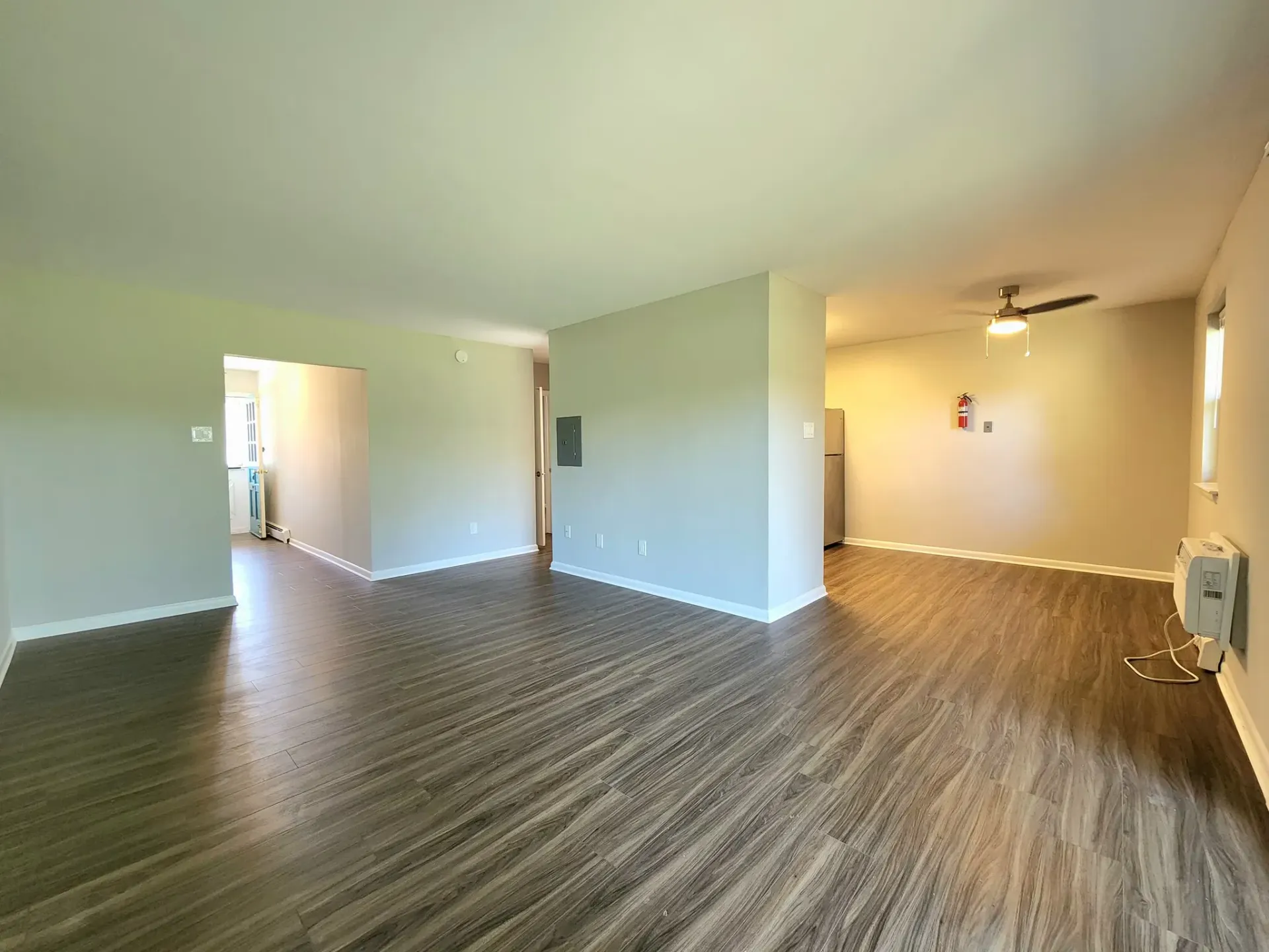 Empty living area in an apartment with wood-look flooring, beige walls, and a ceiling fan.