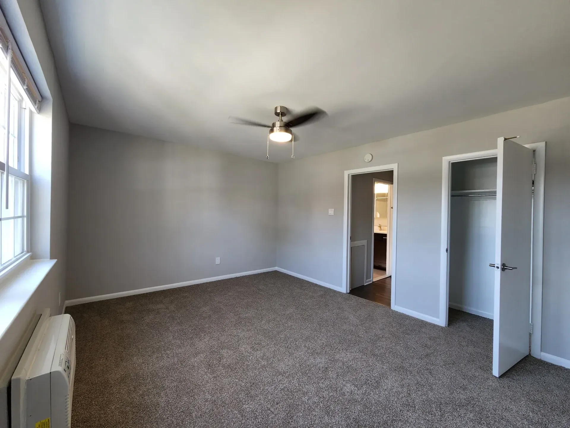 Bedroom with beige walls, carpet, a ceiling fan, large window, and an open closet.