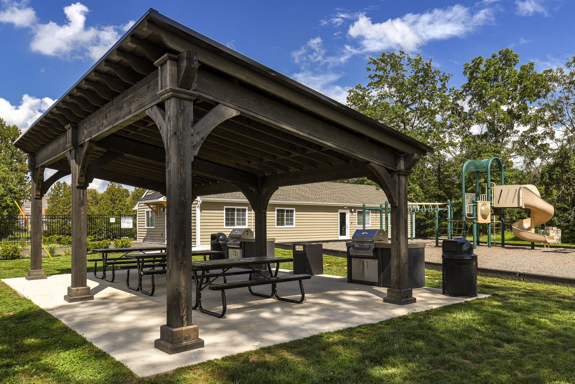 Wooden pavilion with picnic tables and grills at a residential community; playground visible in background.