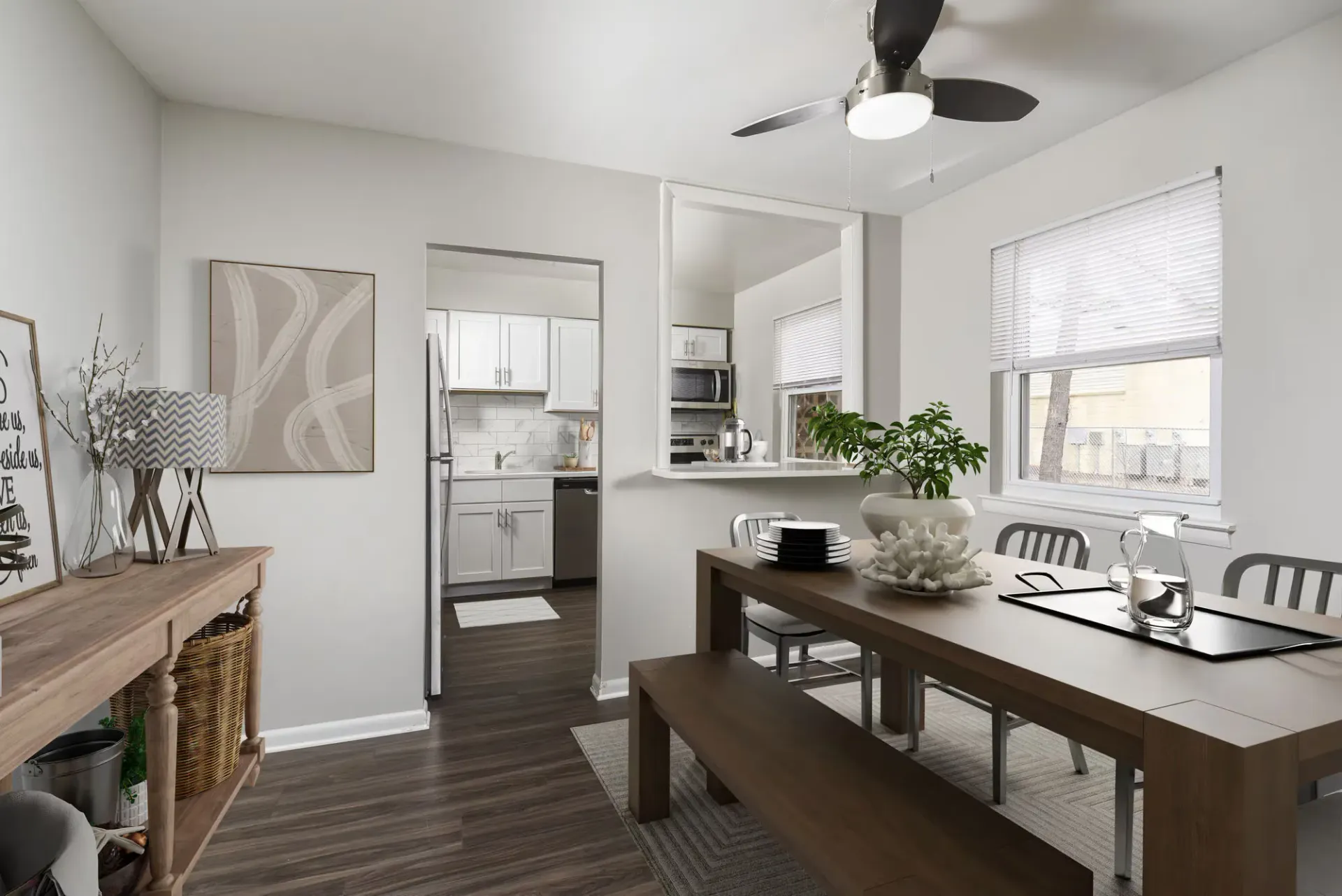Dining area with a long wooden table and bench seating, open to a modern white kitchen.