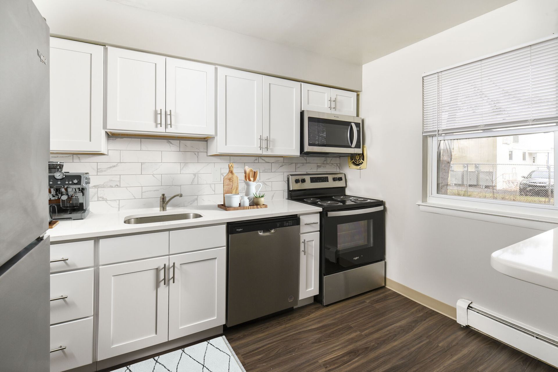 Kitchen in a modern apartment with white cabinets, stainless appliances, and a window.