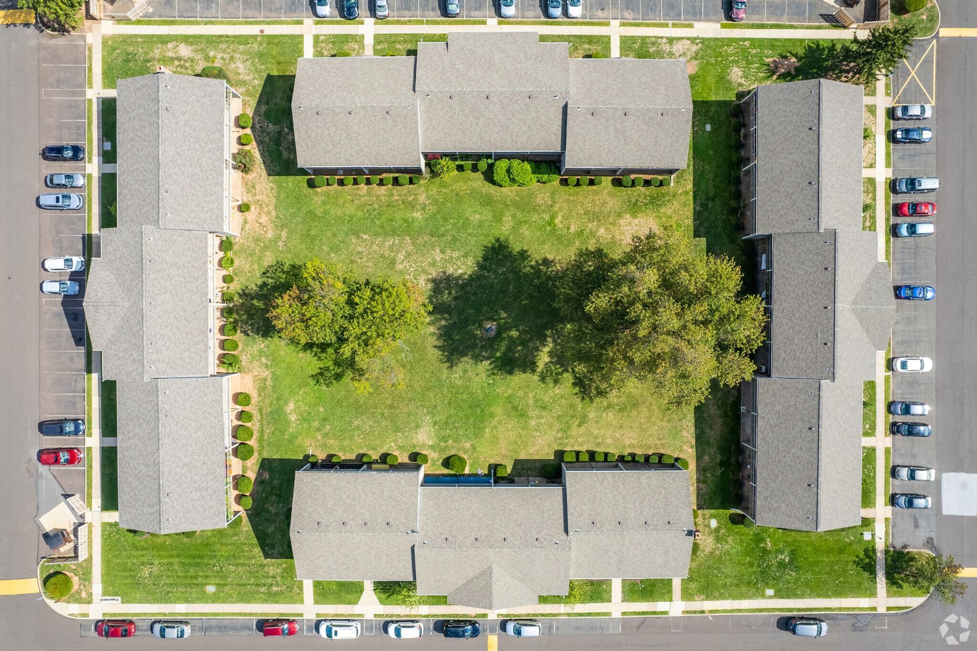 Aerial view of an apartment complex courtyard, with surrounding buildings, trees, and parking.