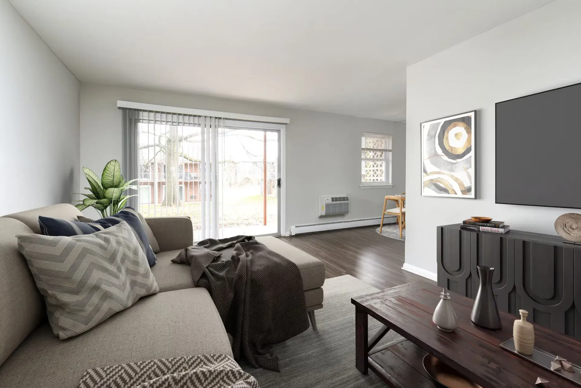 Living room in an apartment with a sectional sofa, plant, coffee table, and sliding glass door.