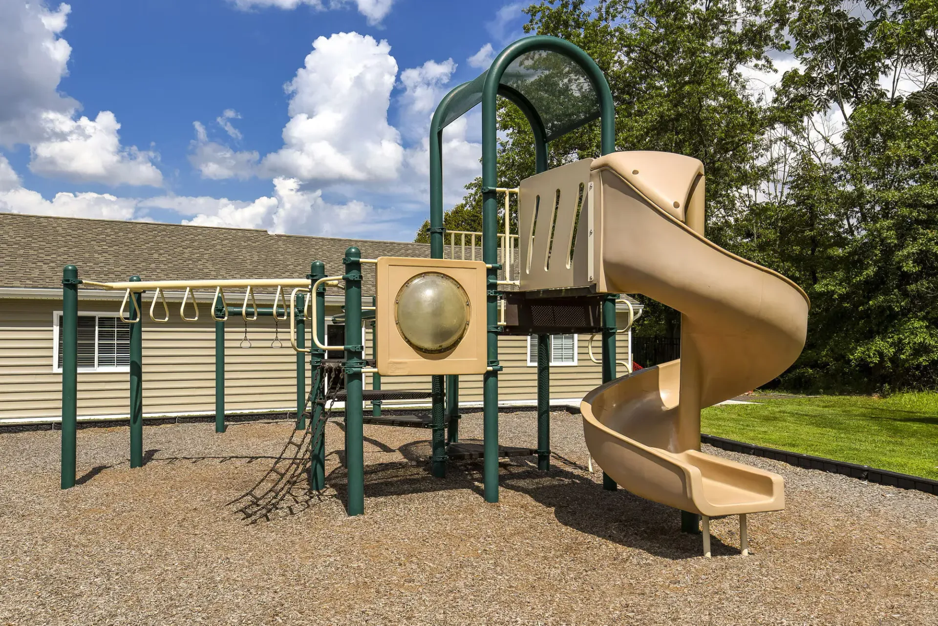 Outdoor playground with beige spiral slide and climbing structure in a residential apartment community.