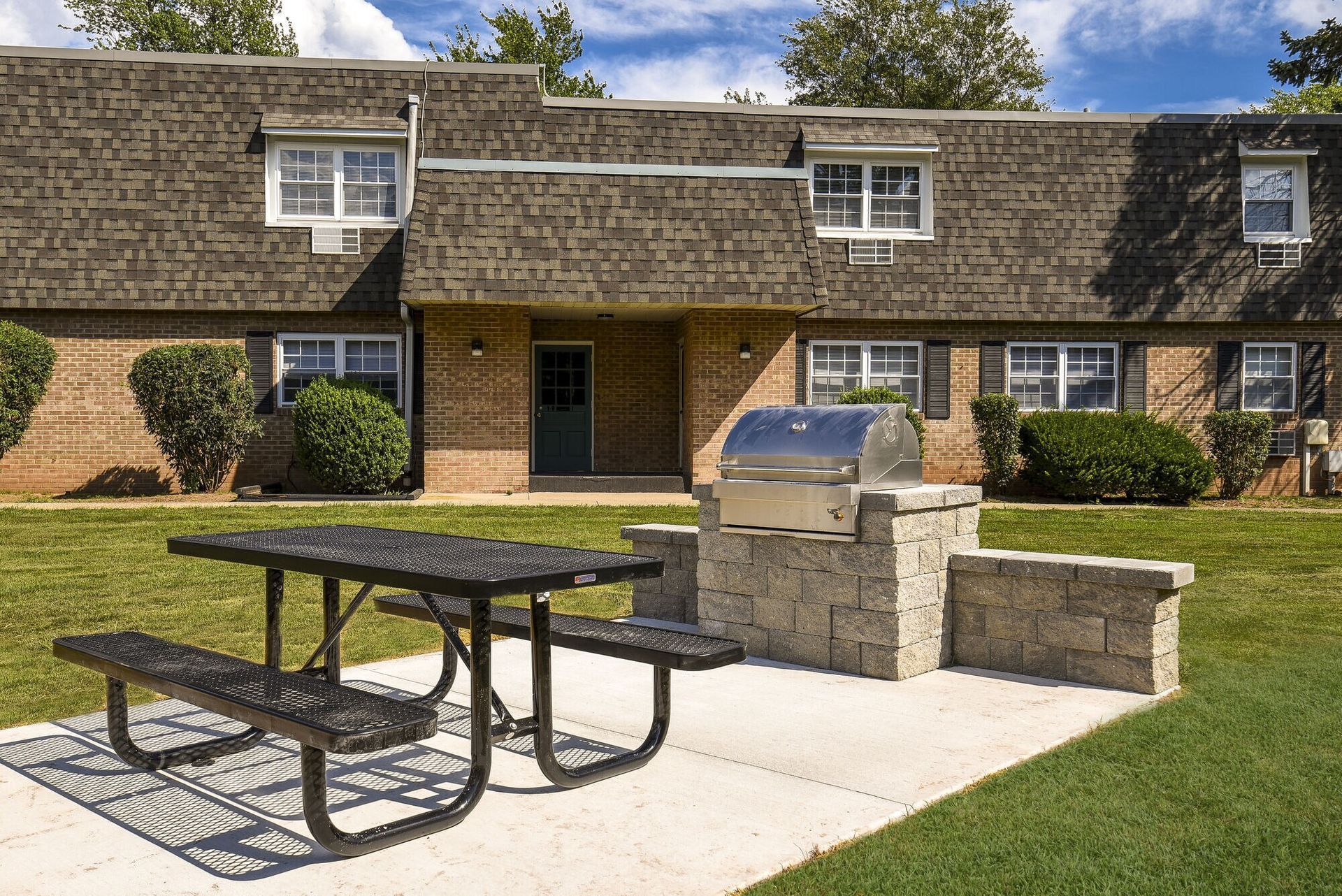 Exterior brick apartment building with a concrete patio, grill, and picnic table.
