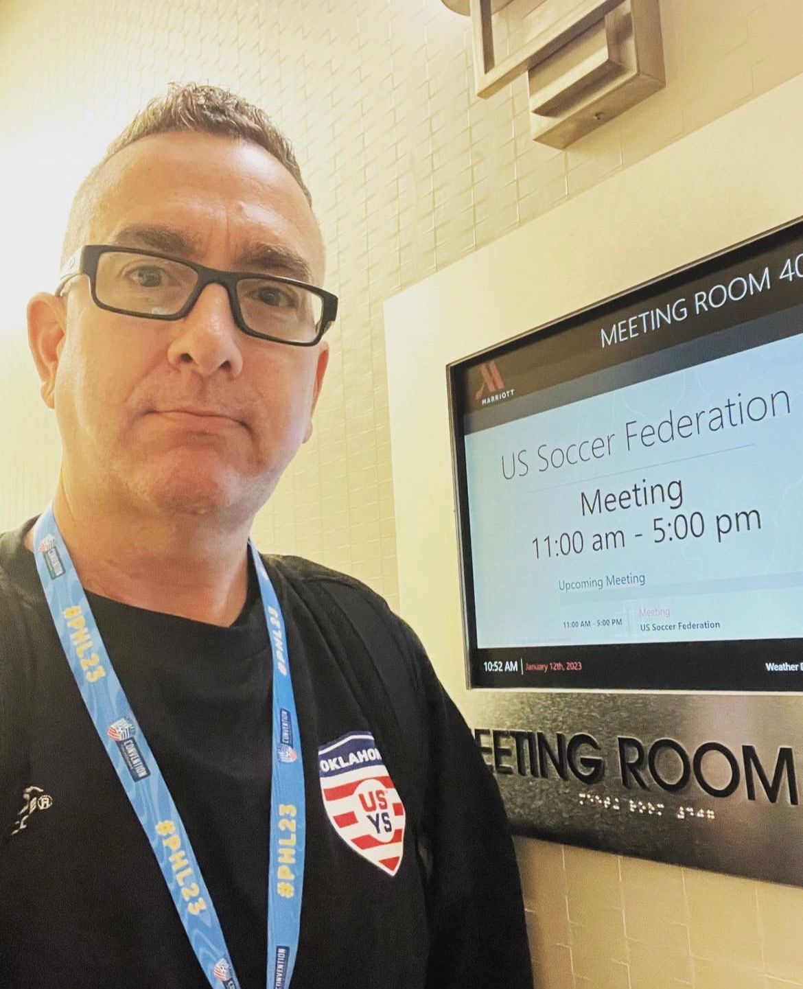 Man with glasses taking selfie in front of a meeting room sign; 