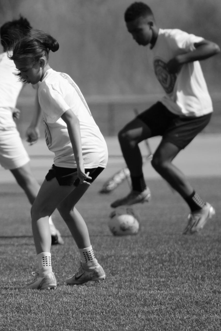 Soccer player in black shirt with white shorts dribbling on a green field.