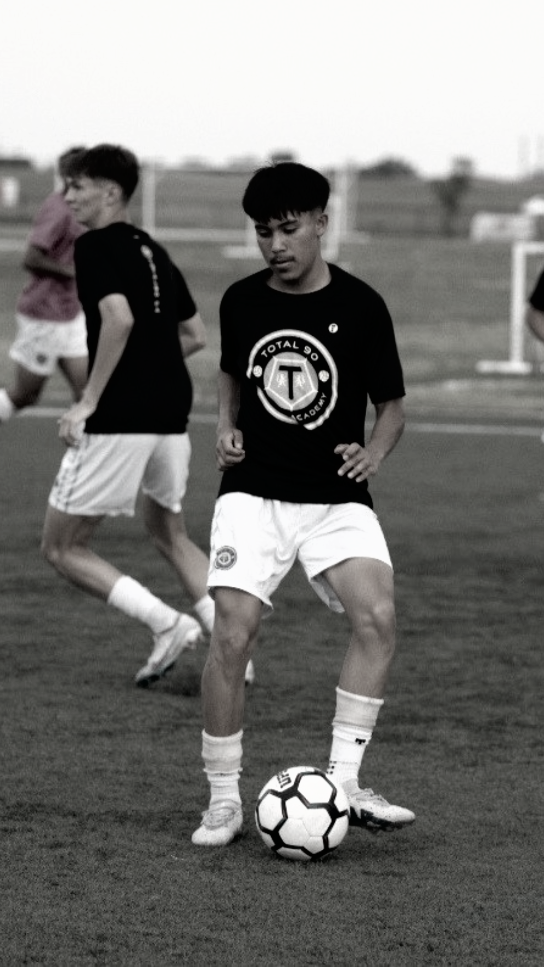 Soccer player in black shirt and white shorts dribbles the ball on a green field.