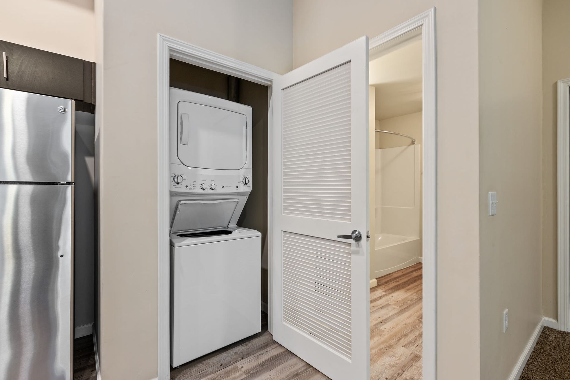 Stacked washer and dryer in a laundry closet beside a doorway to a bathroom.