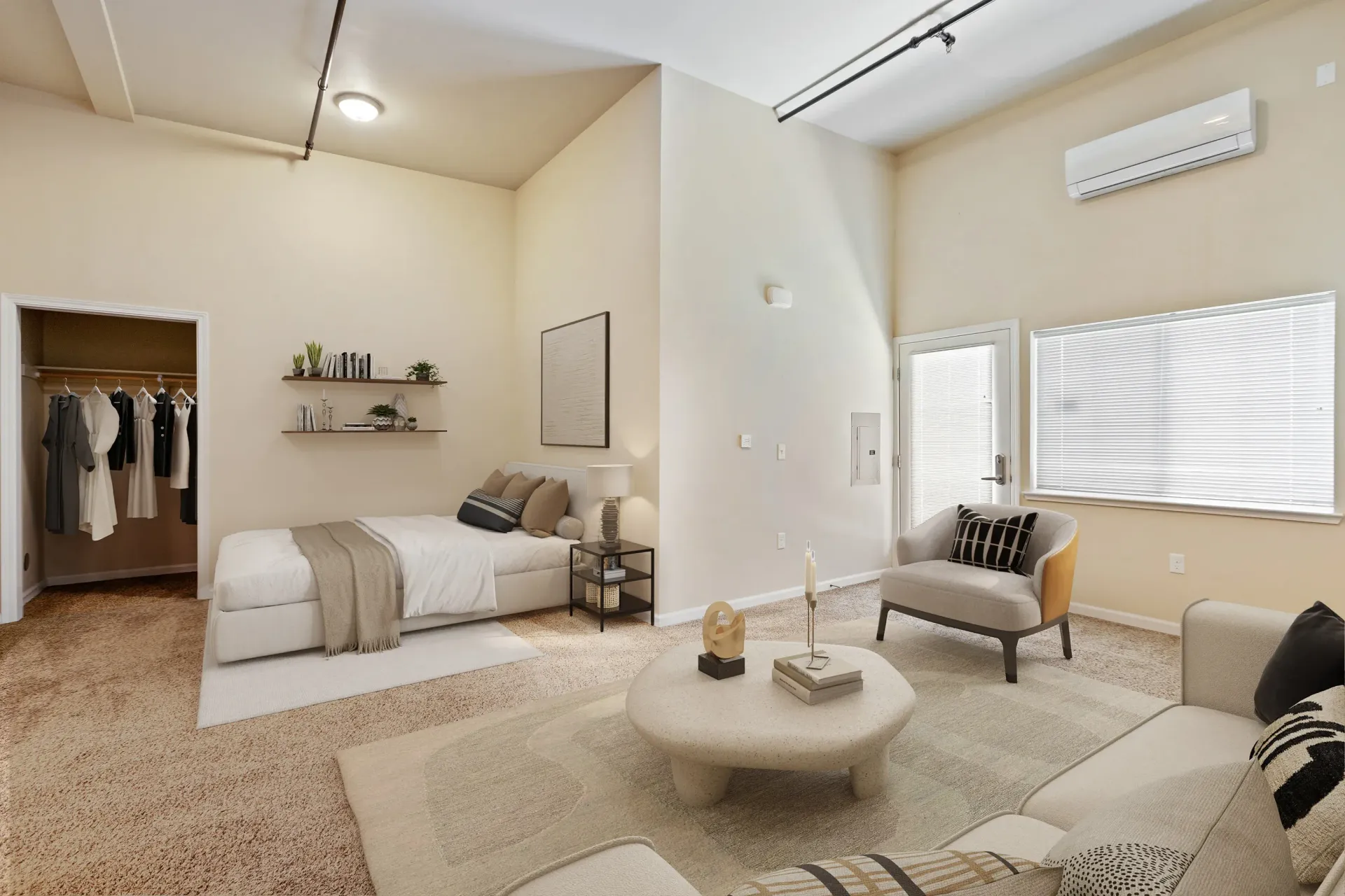 Bedroom and living area in a modern apartment with bed, sofa, coffee table, open closet, and large window.