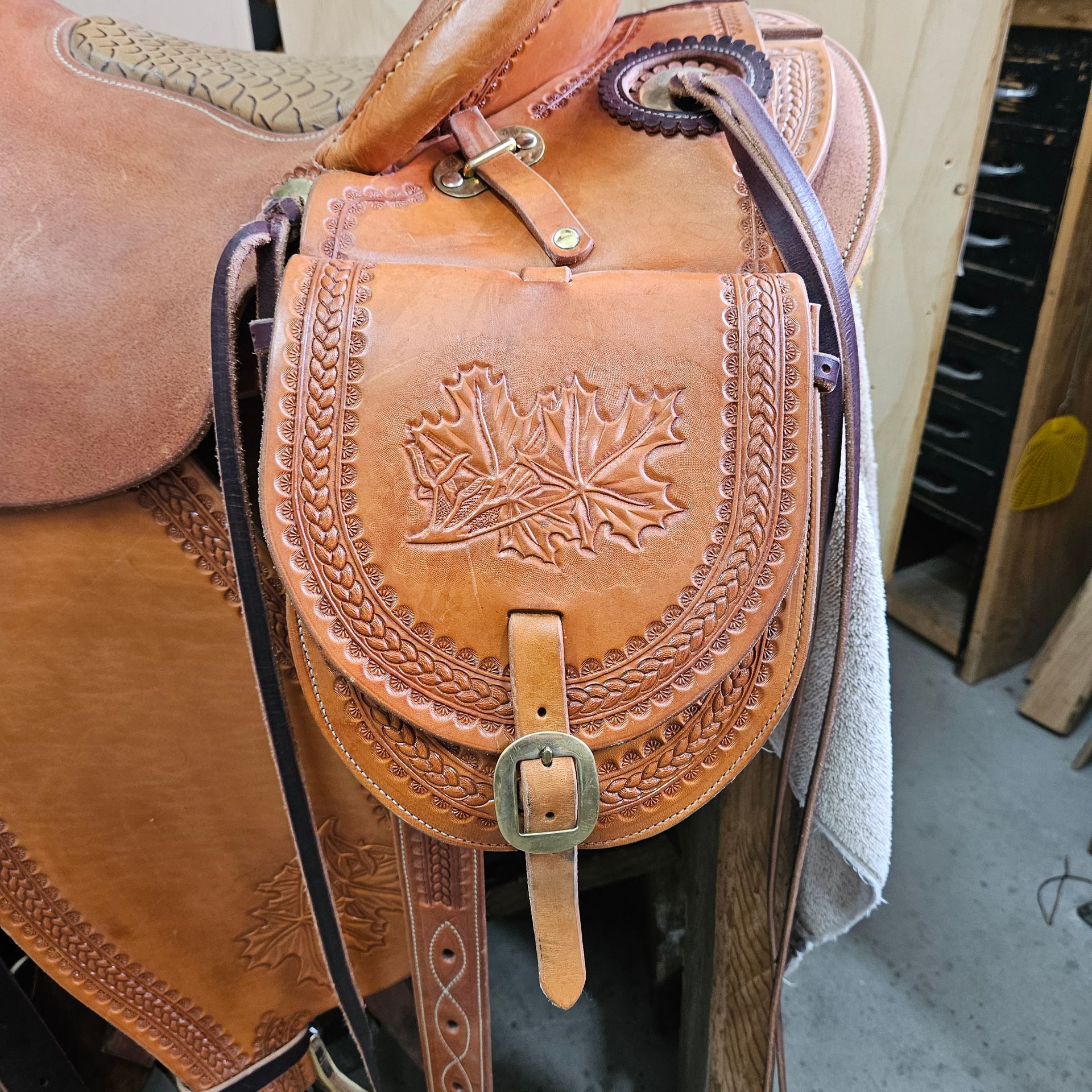 Close-up of a brown leather saddle with tooled accents and a pouch featuring a maple leaf design.