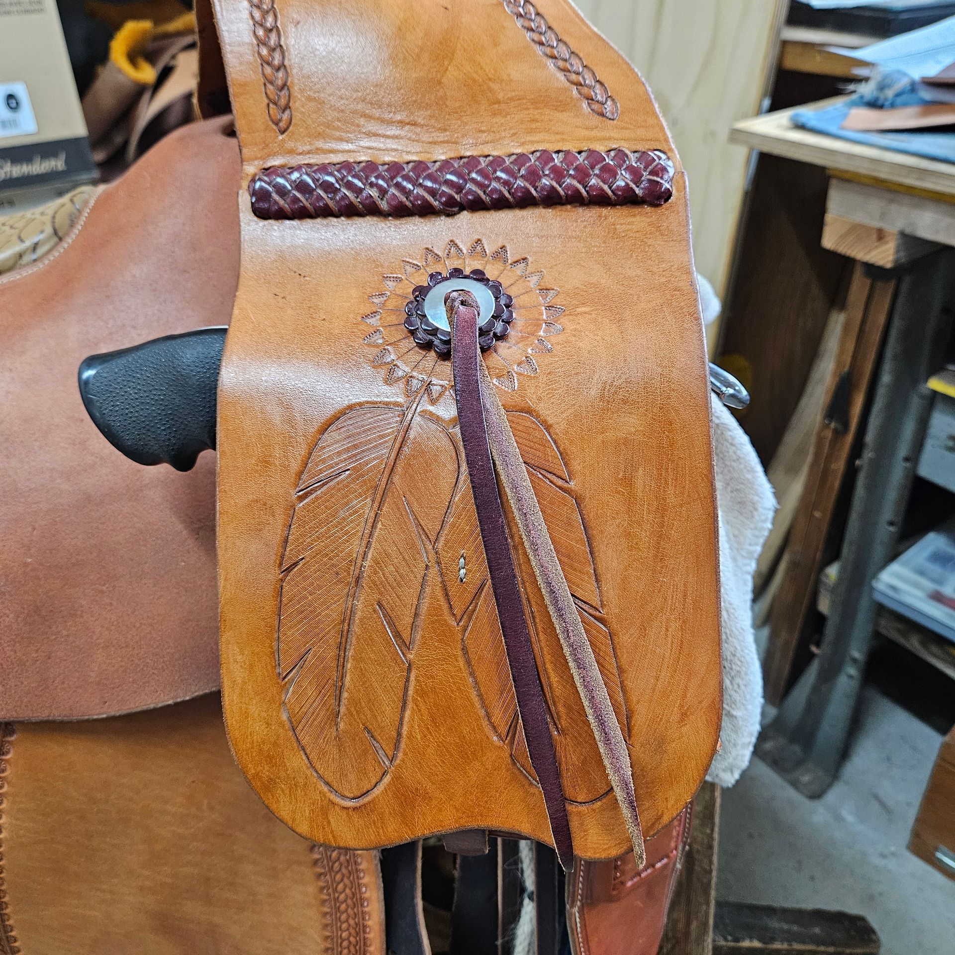 Leather saddle detail with carved feathers and a decorative top. Brown and tan colors.