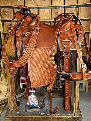 Brown leather Western saddle with tooling, stirrups, and bridle, on a wooden stand.