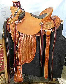 Leather Western saddle with embossed details and stirrups, displayed on a black blanket.