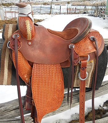 Brown leather western saddle on a fence, snowy background.