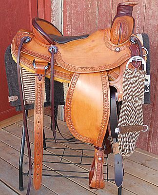 Tan leather western saddle on a rack, showing tooling detail.