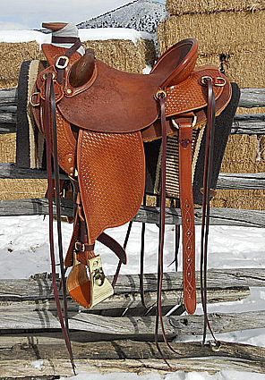 Brown leather western saddle on a fence in a snowy outdoor setting.