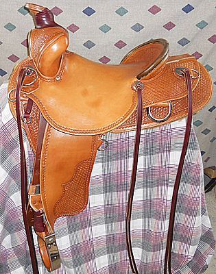 Tan leather Western horse saddle with detailed tooling and stirrups.