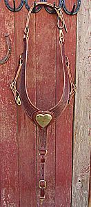 Brown leather horse breast collar with heart-shaped plate hanging on a red wooden wall.
