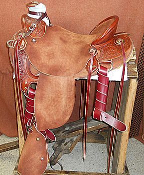 Brown leather Western saddle on a wooden stand, showcasing tooling and red accents.