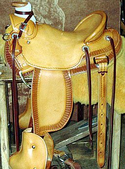 Tan leather western saddle with dark brown accents and straps.