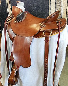 Brown leather Western saddle on white cloth; decorative tooling; golden hardware.