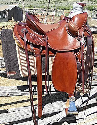 Brown leather Western saddle with stirrups, horn, and skirt, resting on a saddle pad outdoors.