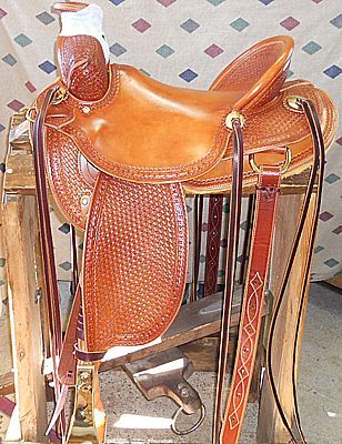 Brown leather western saddle on a wooden stand; basket weave pattern, stirrups hanging.