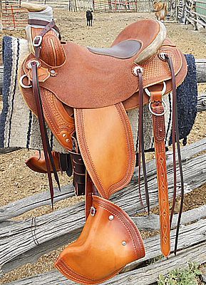 Brown leather Western saddle hanging on a wooden fence outdoors.