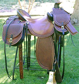 Brown leather western saddle on a metal stand, outdoors on grass.