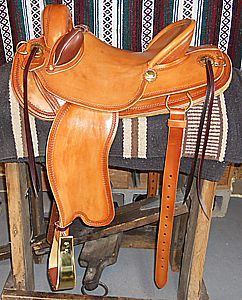 Tan leather western saddle on a wooden stand, resting on a patterned blanket.