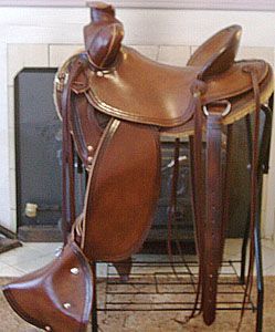 Brown leather Western saddle displayed on a metal stand, in front of a fireplace.