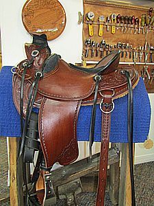 Brown leather horse saddle on a wooden stand, with tools in the background.