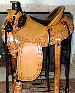 Tan leather western saddle, black seat, intricate tooling, on a black rack.