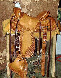 Tan leather western saddle on a wooden stand, with detailed tooling and stirrups.