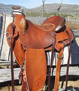 Brown leather western saddle with intricate tooling, outdoors.