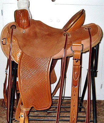 Brown western saddle on a black stand; tan seat, tooled leather details, stirrups hanging.