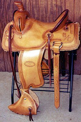 Tan leather Western saddle on a black metal stand against a wooden backdrop.