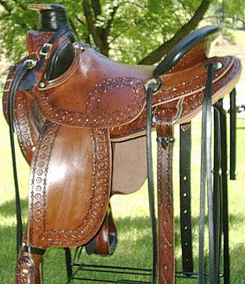 Brown leather Western saddle with tooling, on a black stand.