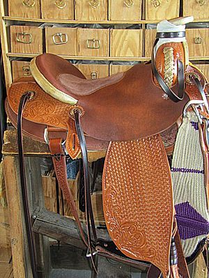 Brown leather saddle with decorative tooling, on a wooden stand.
