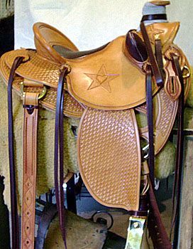 Tan leather western saddle with star design, tooled texture, and hanging stirrups.