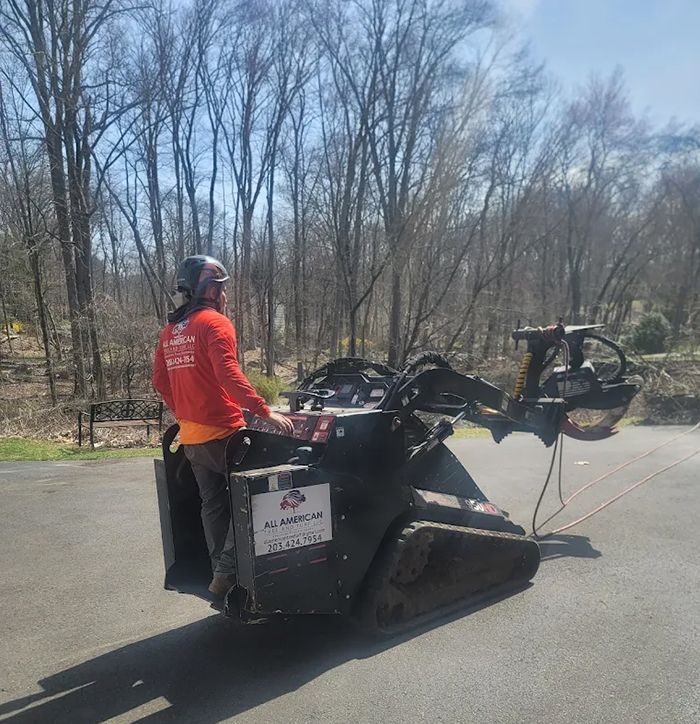 Person operating a stump grinder, wearing safety gear, outdoors.