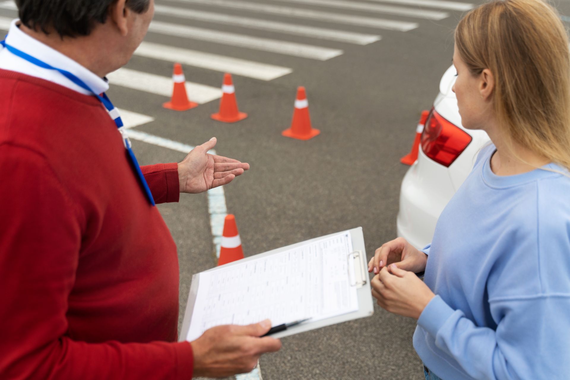 A man is talking to a woman in front of a car while holding a clipboard.