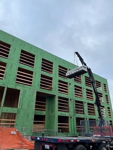 A crane is lifting a large piece of wood in front of a building under construction.