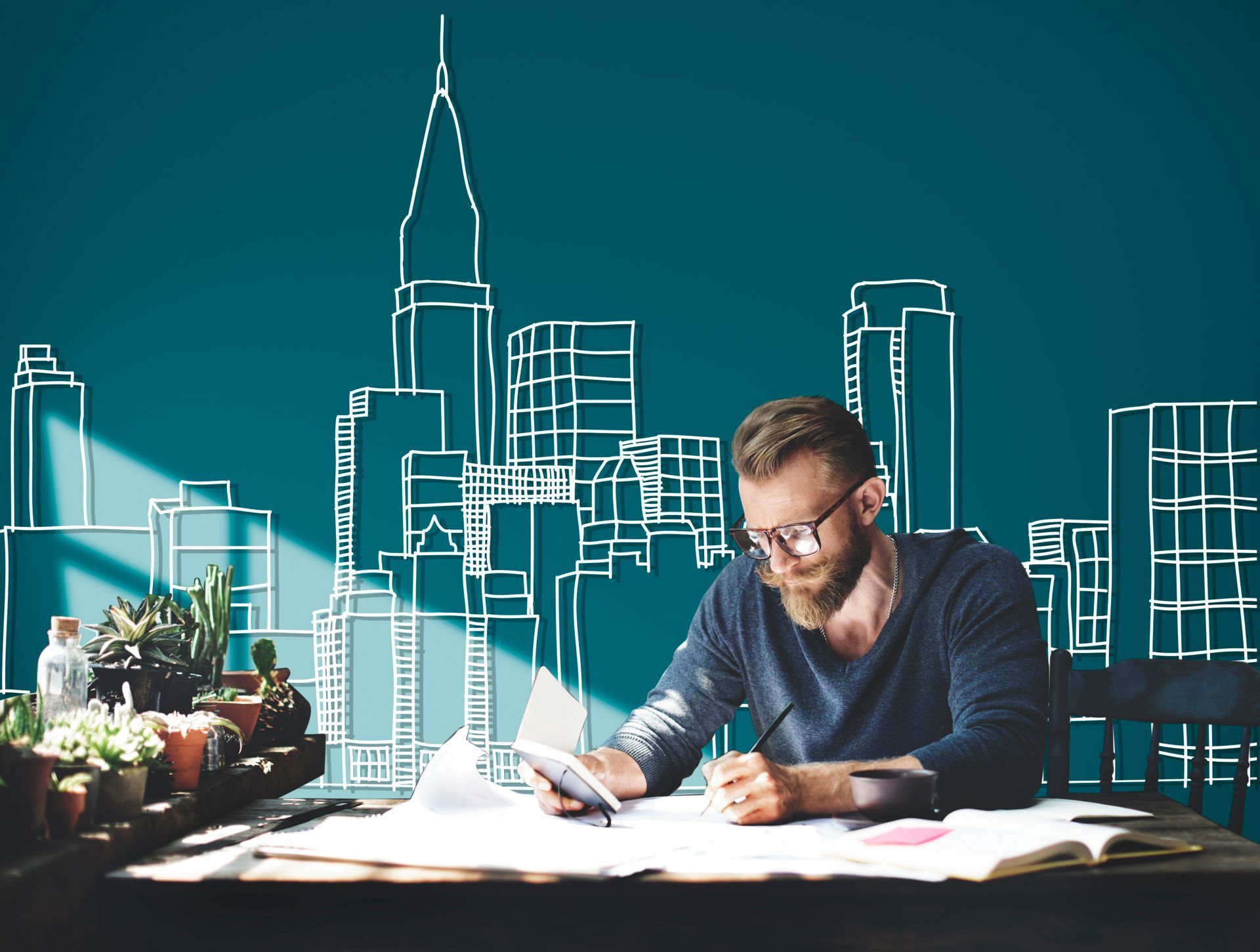 A man is sitting at a desk with a drawing of a city on the wall behind him.