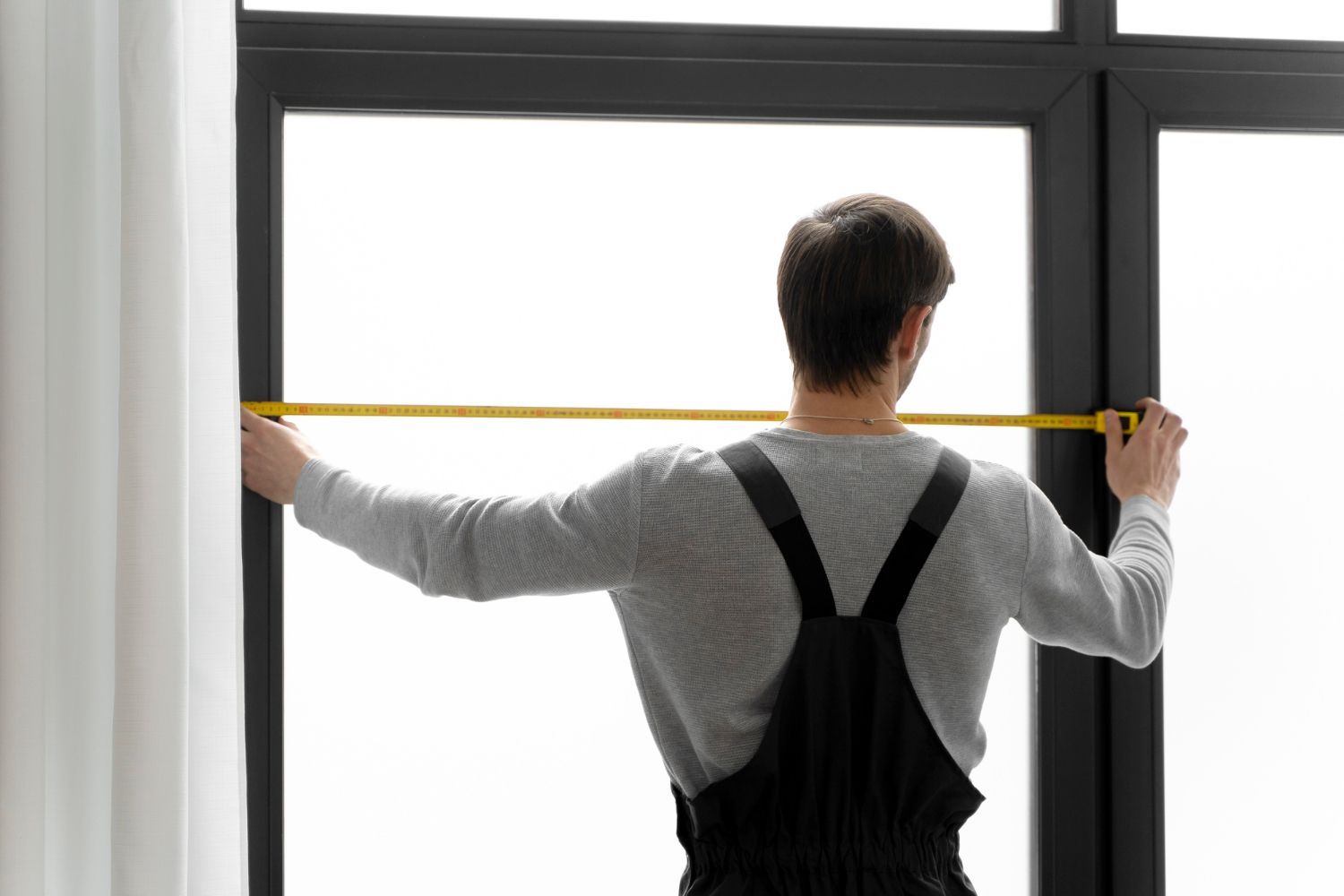 A man is measuring a window with a tape measure.