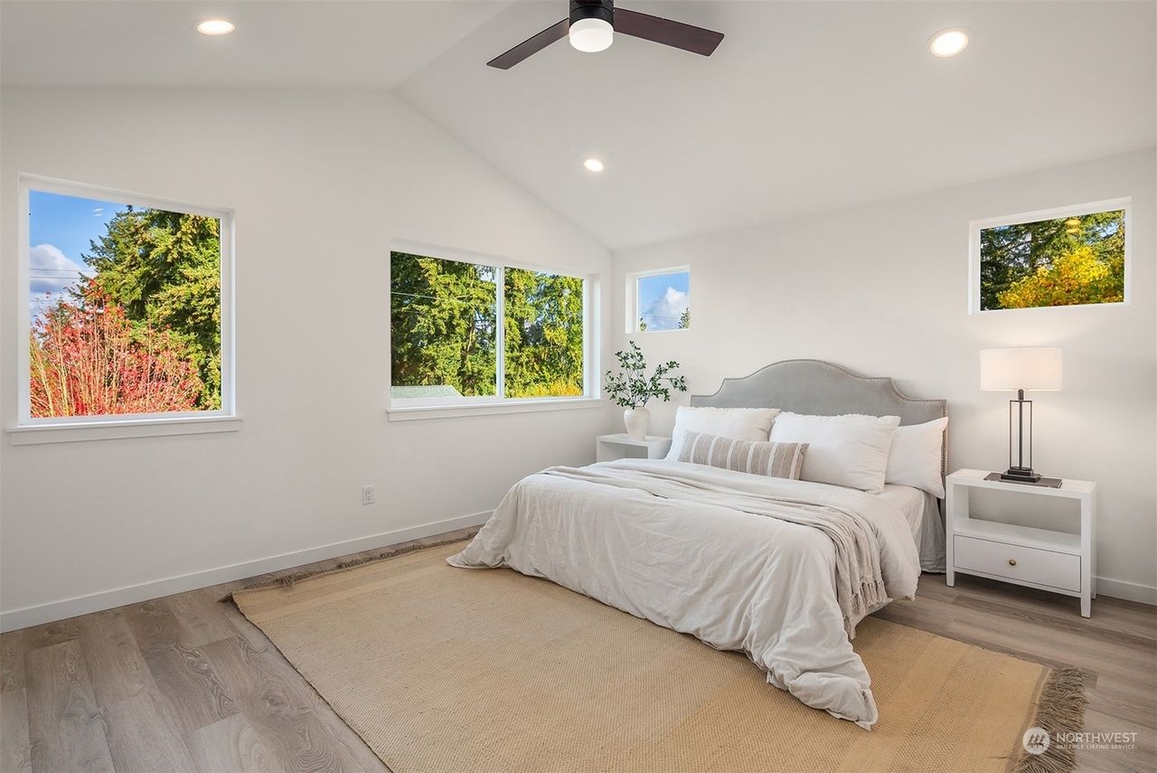 A bedroom with a bed , nightstand , ceiling fan and two windows.