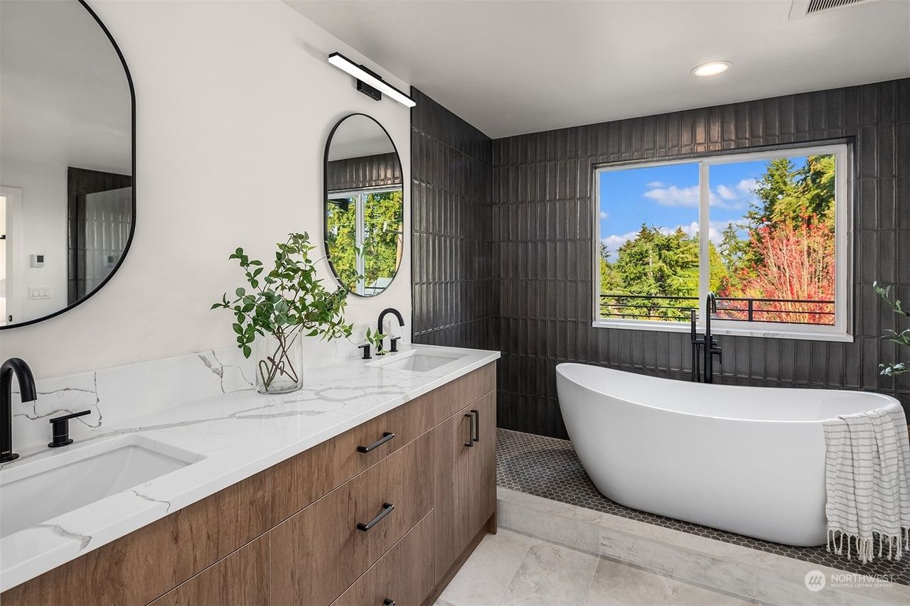 A bathroom with a tub , sinks , mirrors and a window.